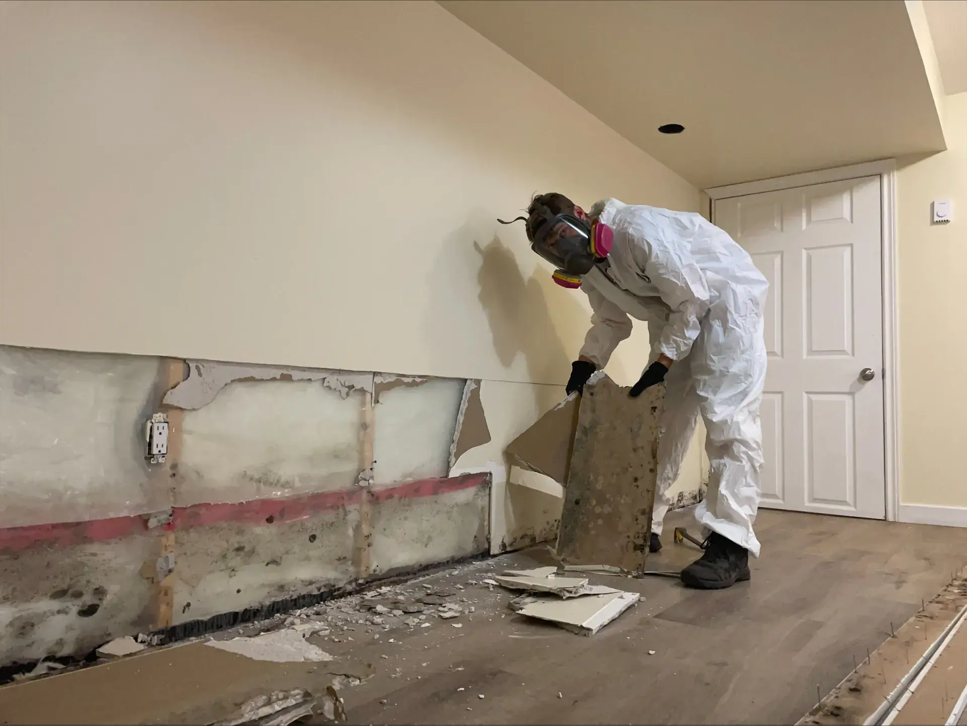 Andrew in full PPE and respirator removing mould-damaged drywall during AMRT certified remediation in a Central Alberta basement
